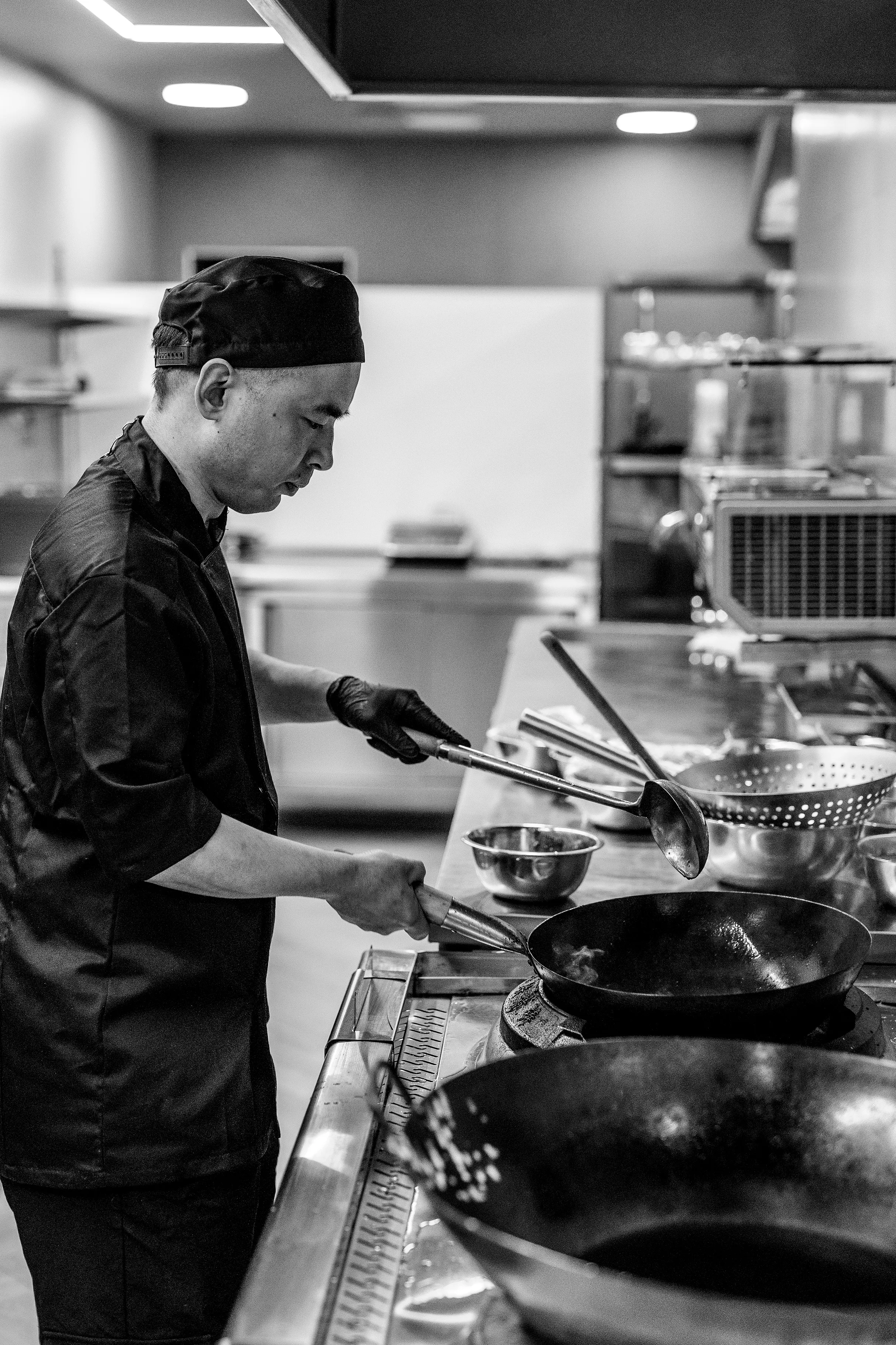 Virėjas ruošia patiekalą wok keptuvėje, nespalvota nuotrauka