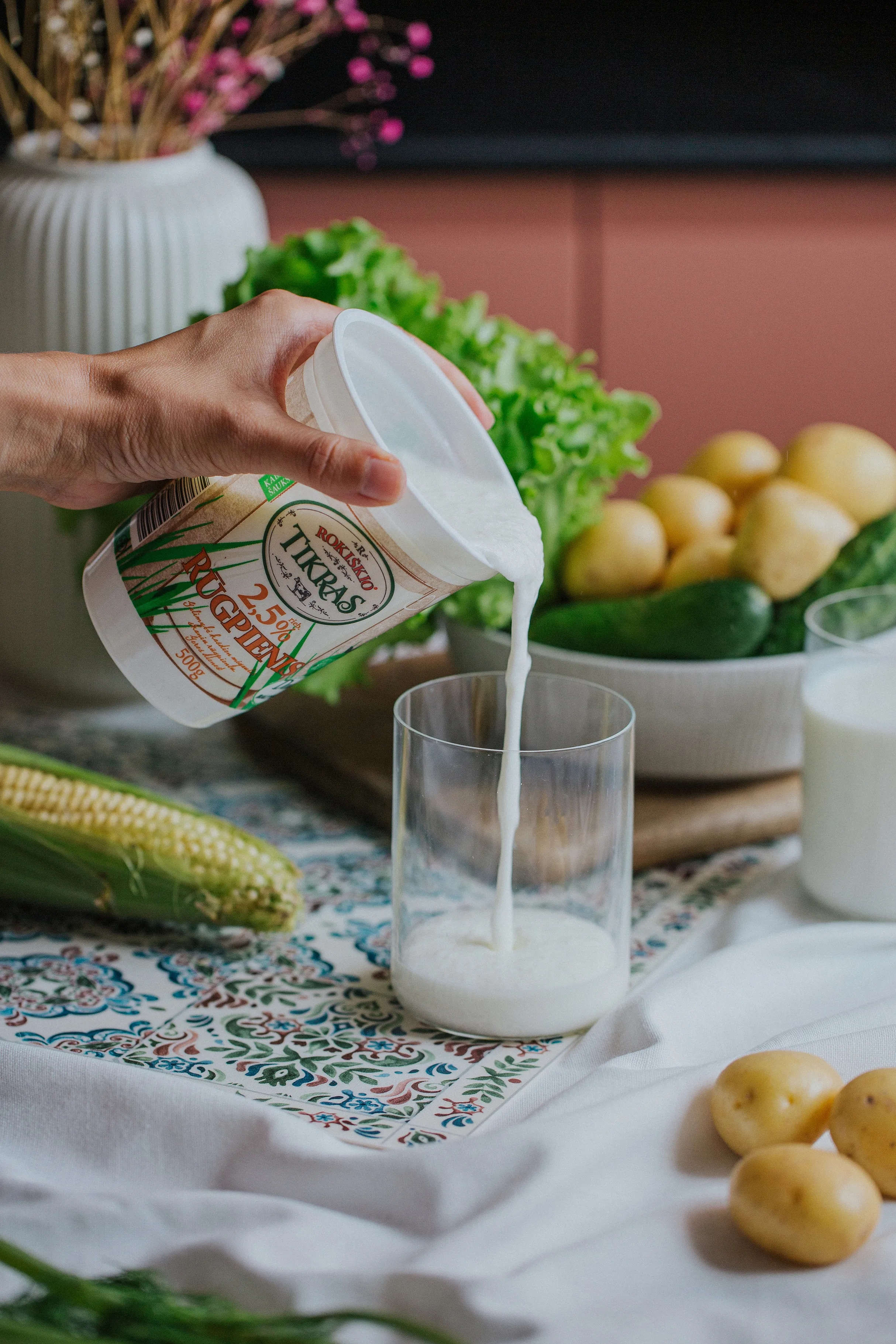Pienas pilamas į stiklinę prie šviežių daržovių