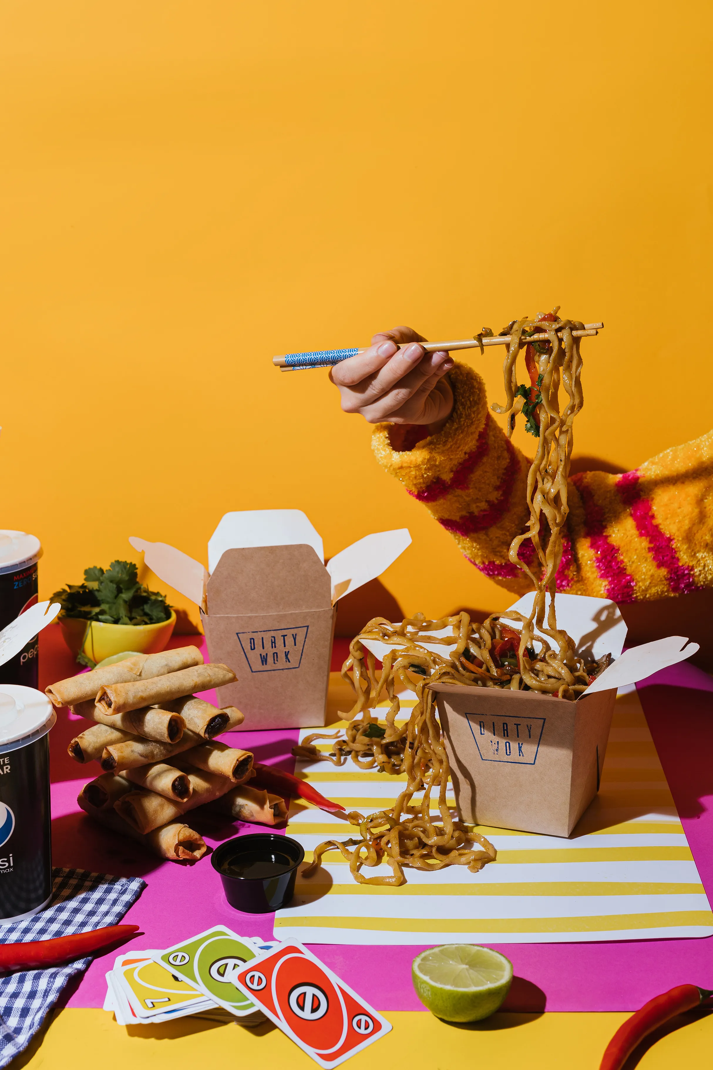 Makaronai keliami lazdelėmis iš išsinešimo dėžutės ryškiame fone