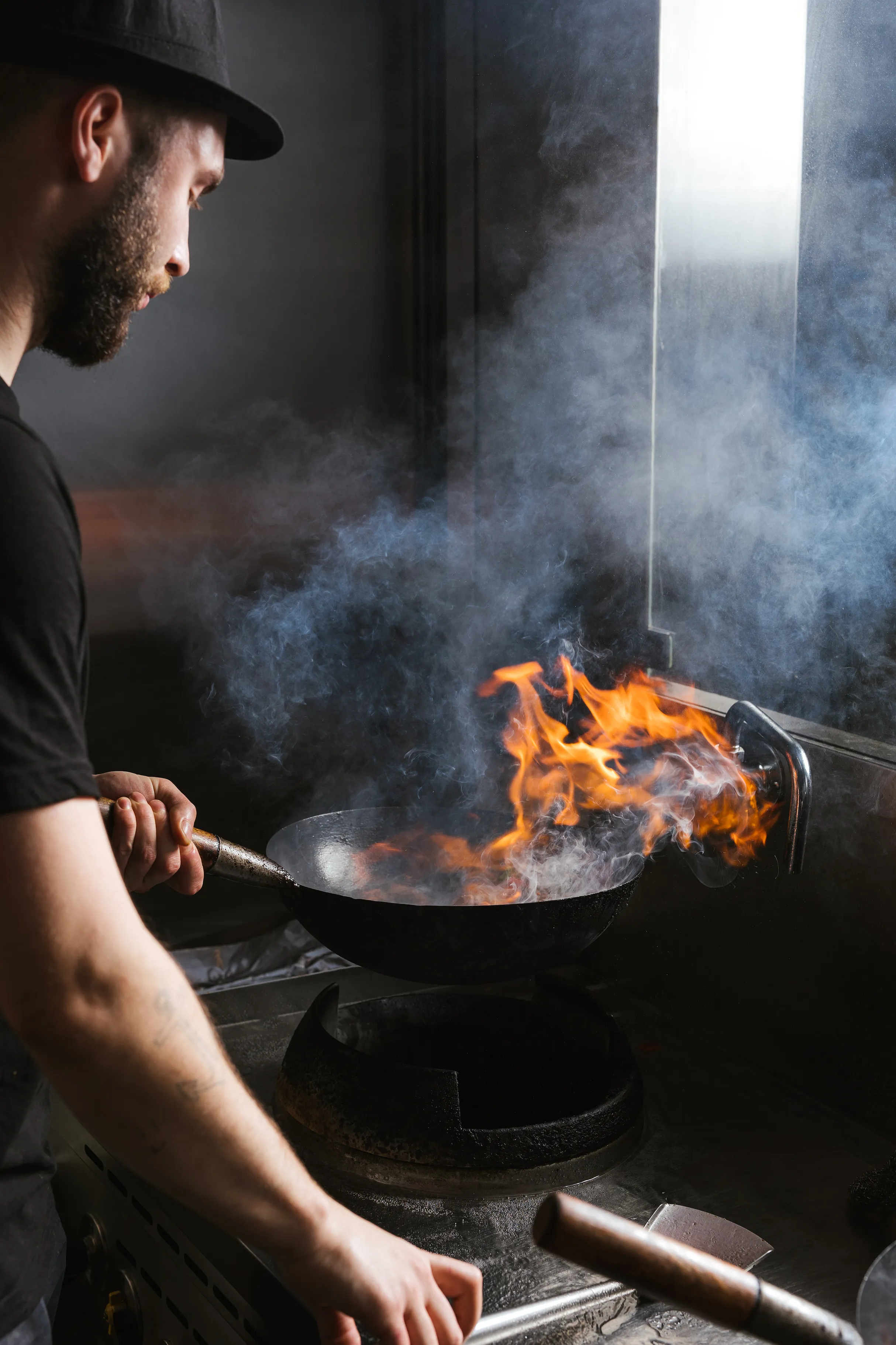 Virėjas ruošia patiekalą liepsnojančioje wok keptuvėje