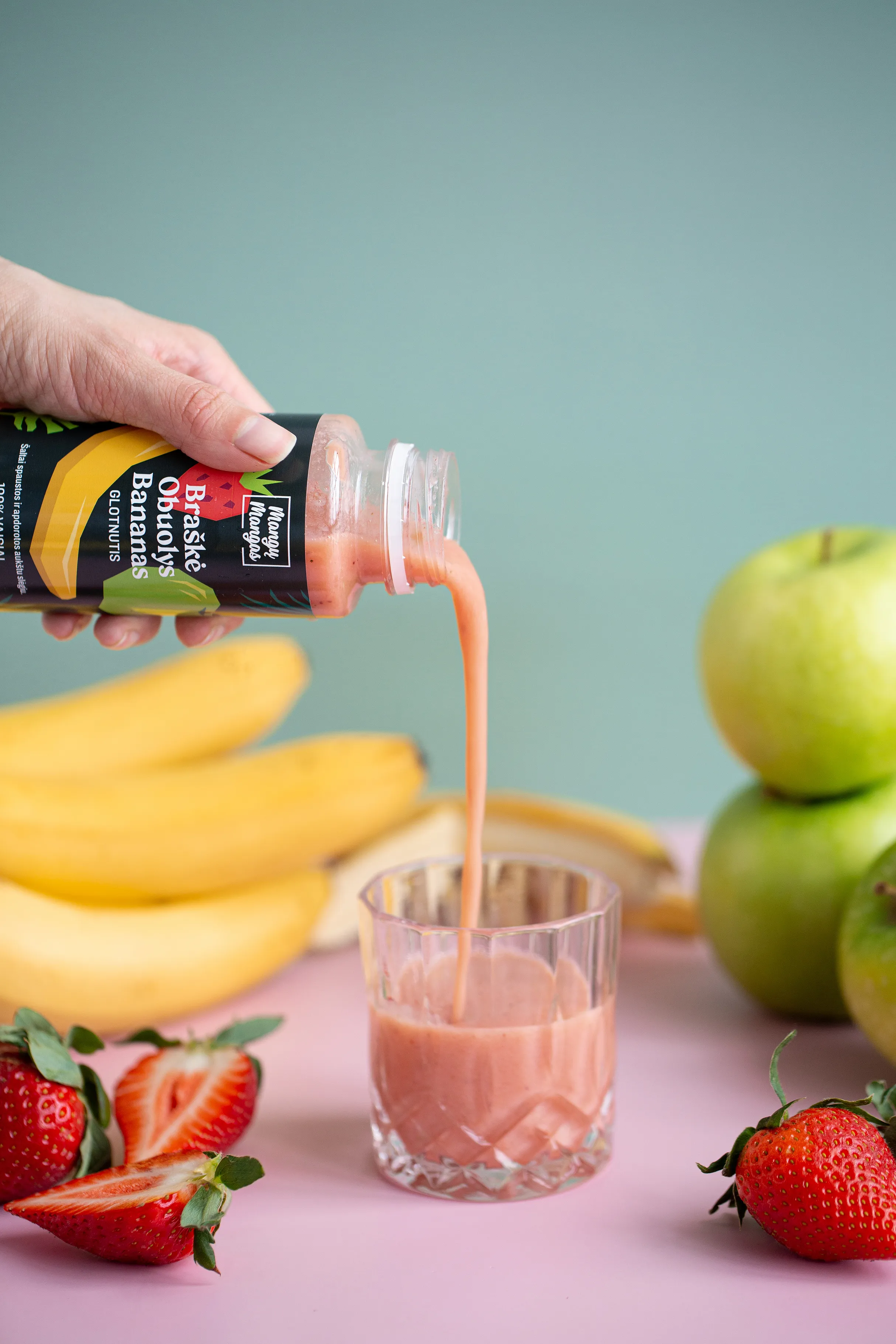 Vaisių sultys pilamos į stiklinę prie bananų ir obuolių